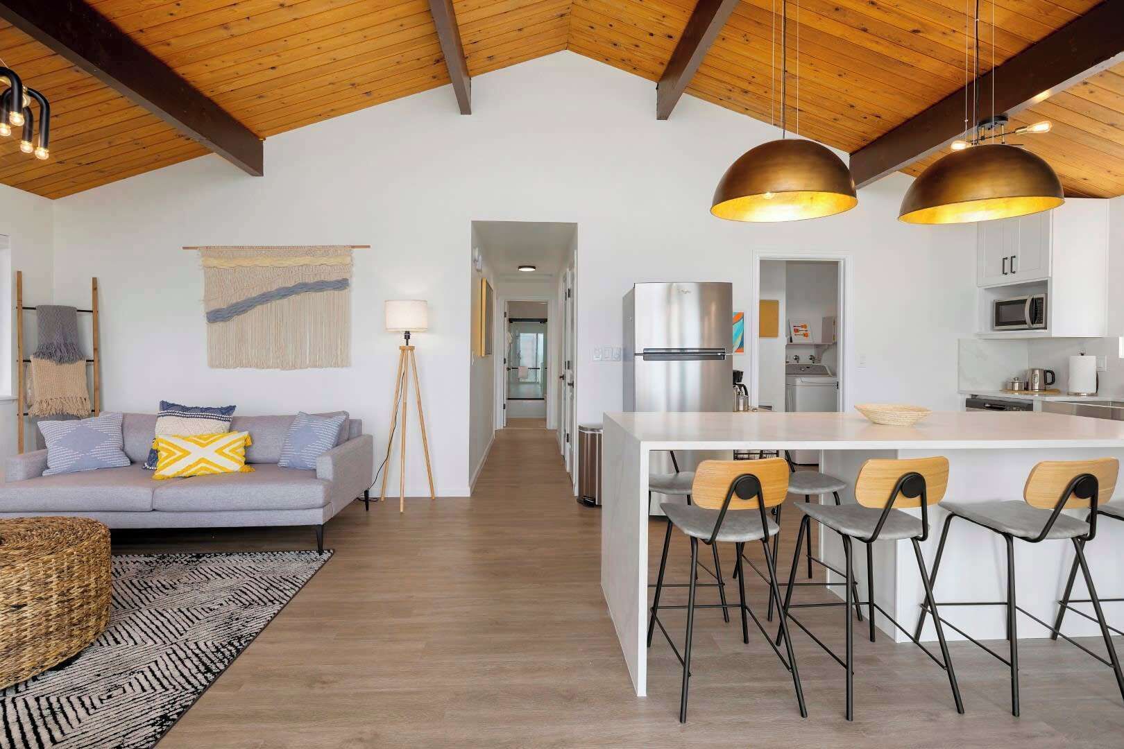 A modern kitchen with a central island, bar stools, and a dining area with a sofa and lamp.