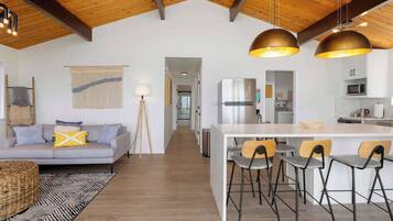A modern kitchen with a central island, bar stools, and a dining area with a sofa and lamp.