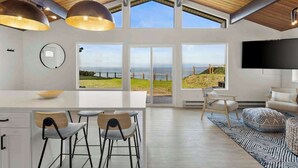 Una cocina moderna con una isla grande, taburetes de bar y vista al mar a través de amplios ventanales.