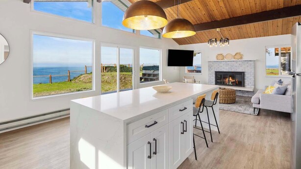 Una cocina moderna con una isla grande, armarios blancos y vista al océano.