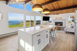 A modern kitchen with a large island, white cabinetry, and a view of the ocean. - Island Hideaway with Stunning Ocean Views (Oak Harbor)