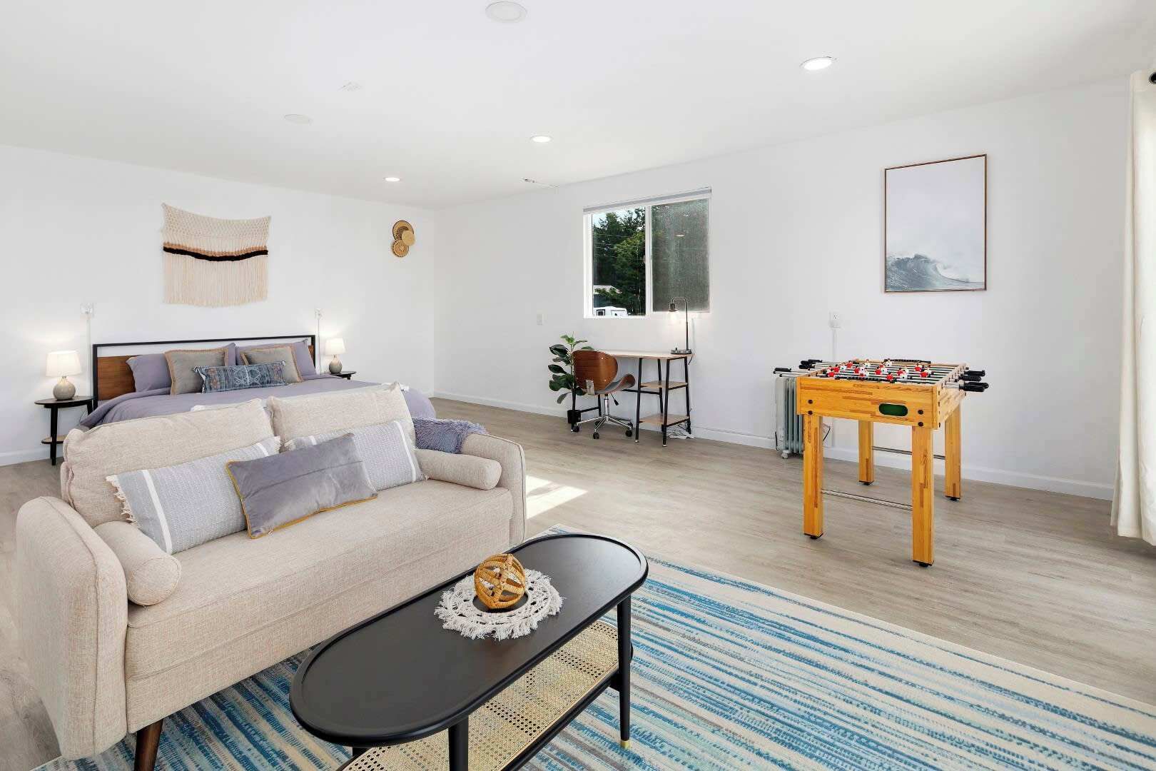 A modern living room with a sofa, a coffee table, a foosball table, and a desk with a chair.