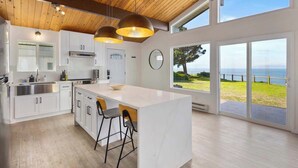 Una cocina moderna con armarios blancos, una isla grande con taburetes de bar y vistas al mar a través de amplios ventanales.
