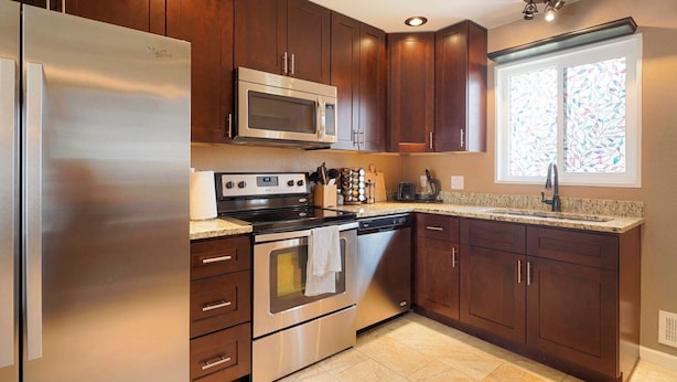 A kitchen with stainless steel appliances, dark wooden cabinets, a granite countertop, and a window with stained glass. - Cozy Getaway Retreat 4BR At Northglenn (Northglenn)