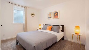 A bedroom with a bed, bedside lamps, a window with curtains, and two framed pictures on the wall. - Cozy Getaway Retreat 4BR At Northglenn (Northglenn)