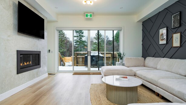 A modern living room with a fireplace, a large sofa, a coffee table, and a flat-screen TV mounted on the wall. - ULTRA LUXURY BLUE ROSE CHALET BUILT IN 2023 HOSTS 12 GUESTS GYM/HOTTUB/GAMES  (blue mountain)