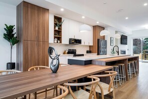 A modern kitchen with wooden cabinets, a central island, bar stools, and pendant lighting.