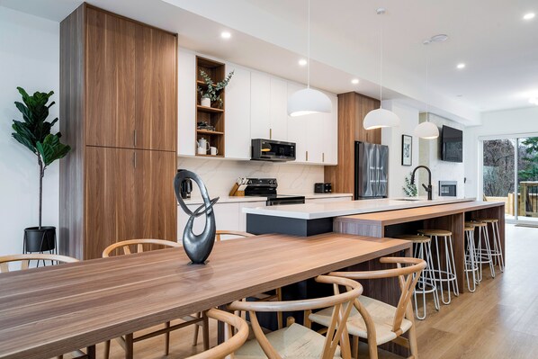 Una cocina moderna con armarios de madera, una isla central, taburetes de bar e iluminación colgante.