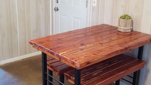 A wooden table with benches in a room with a door and a framed picture on the wall.