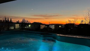 Une piscine au crépuscule, avec vue sur le coucher de soleil, entourée d’immeubles.