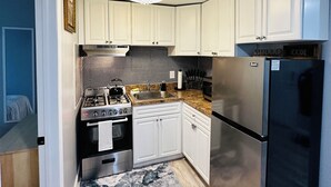 A compact kitchen with white cabinets, a stainless steel refrigerator, a gas stove, and a microwave.