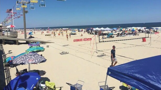 A beach with multiple umbrellas, a lifeguard tower, and a person walking.