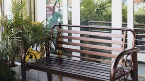 Un banco de madera con reposabrazos de metal, ubicado frente a una ventana de múltiples paneles.