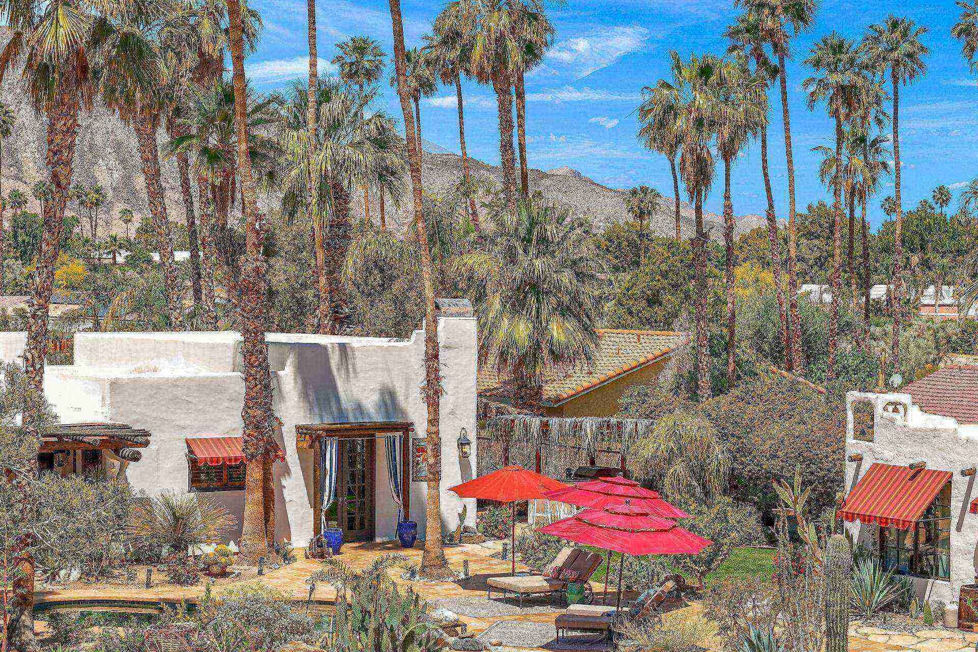 Un patio con palmeras, mobiliario exterior y un edificio con toldo rojo.