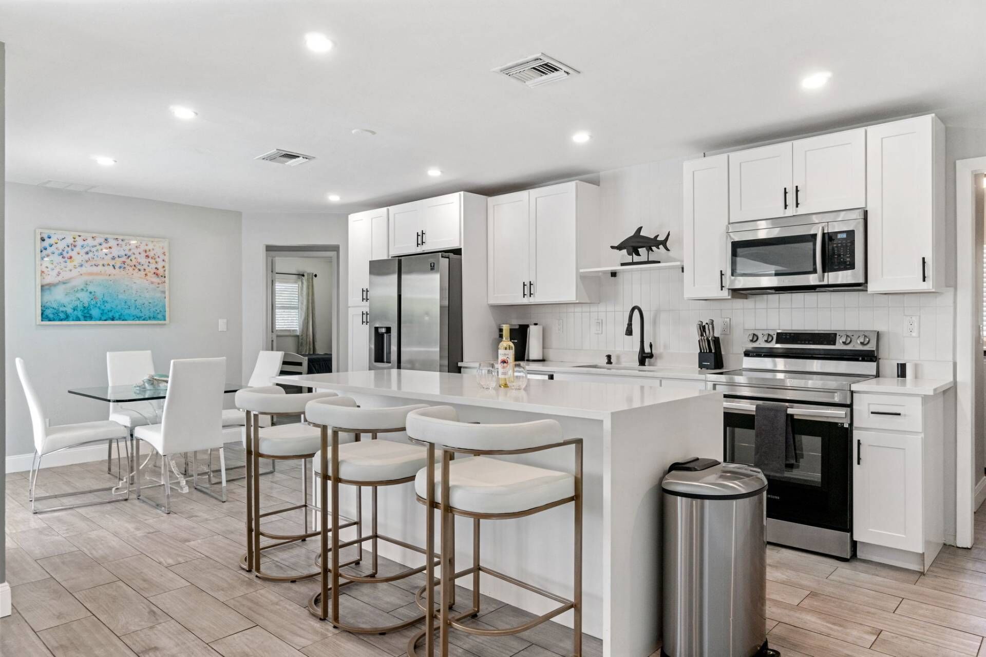 Una cocina moderna con armarios blancos, electrodomésticos de acero inoxidable y una isla central con taburetes de bar.