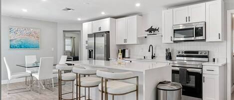 Una cocina moderna con armarios blancos, electrodomésticos de acero inoxidable y una isla central con taburetes de bar.