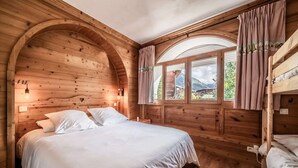 Ein Schlafzimmer einer Holzblockhütte mit einem großen Bett, einem Fenster mit Vorhängen und einem Etagenbett.
