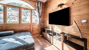 Ein gemütlicher Raum mit Holzwänden, einem großen Fenster mit Blick auf Gebäude, einem wandmontierten Flachbildfernseher und einem Sofa mit Kissen.