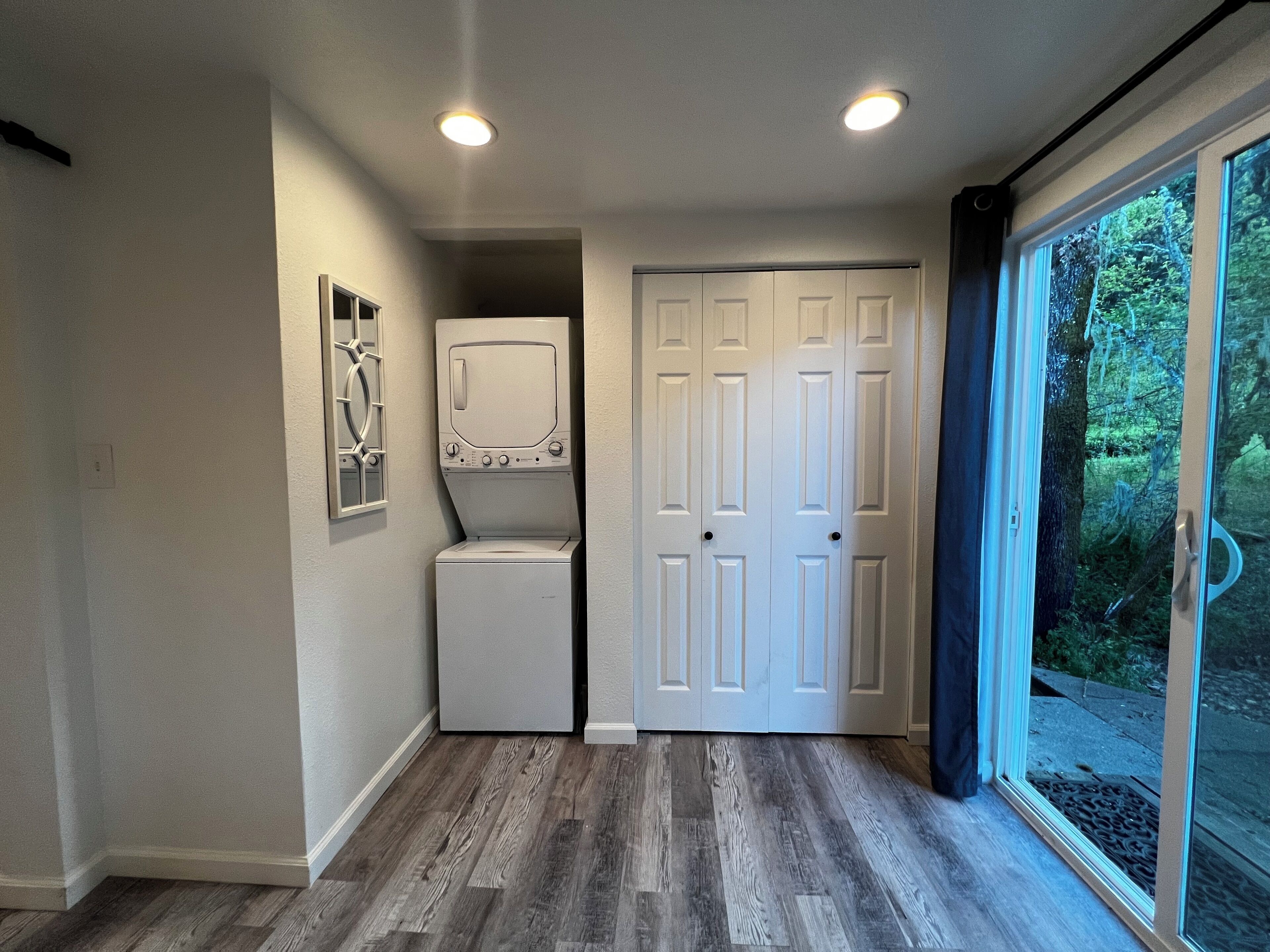 A laundry room with a washer and dryer, a door, and a window with a view of greenery.