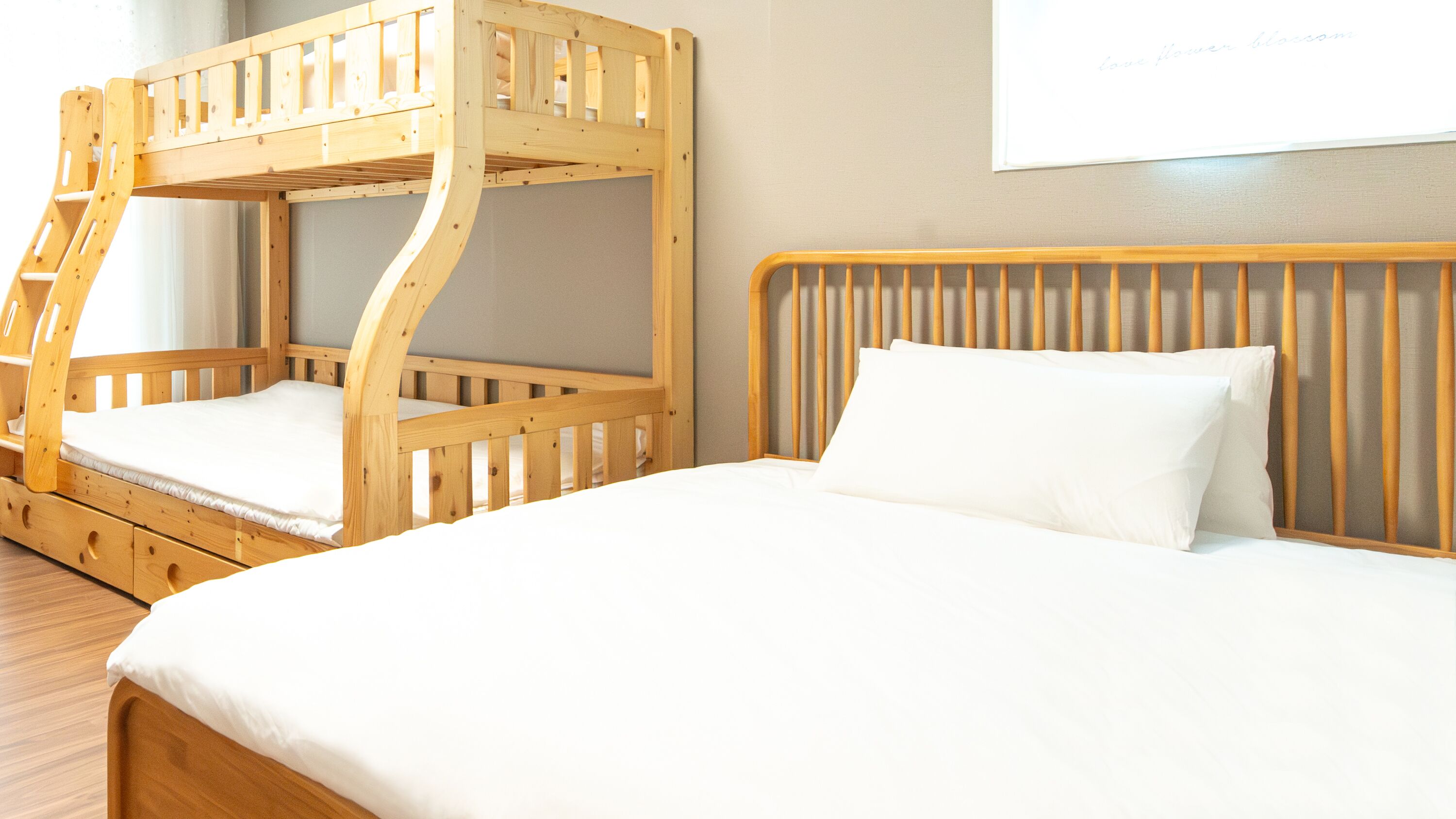 Une chambre avec un lit superposé et un lit simple, tous deux dotés d’une structure en bois et de draps blancs.