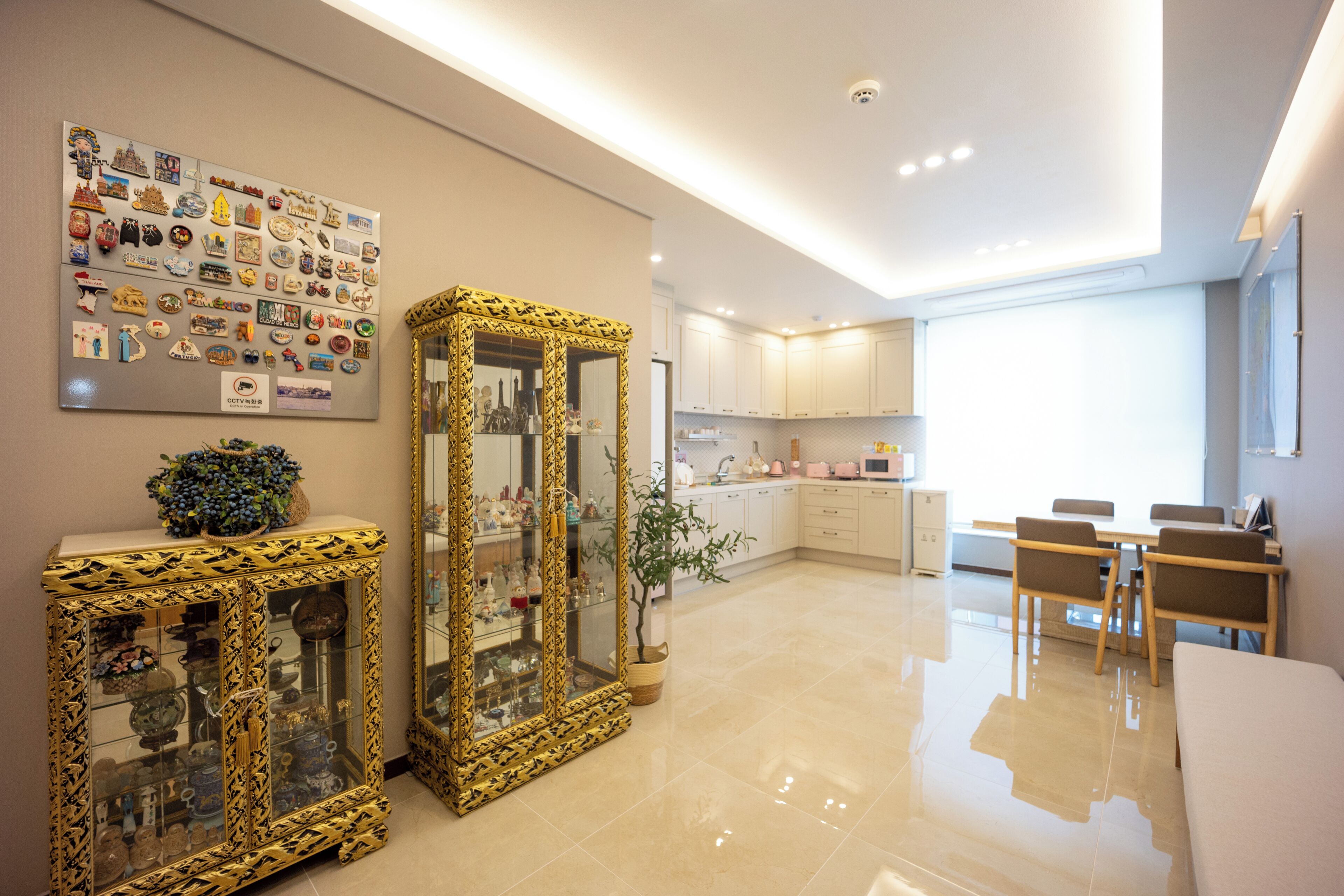 A modern kitchen with white cabinets, a dining area with wooden chairs, and a decorative mirror with a gold frame.