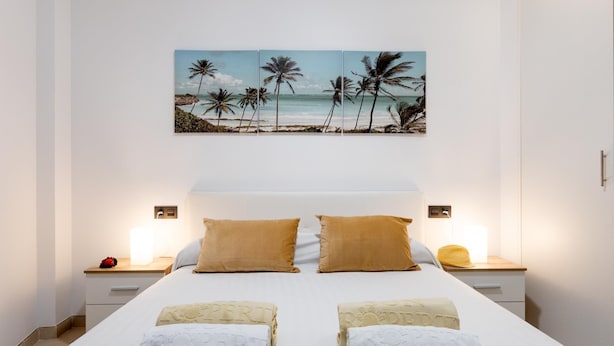 Une chambre d’hôtel avec un lit, deux tables de chevet, un tableau représentant une scène de plage et des serviettes sur lesquelles est inscrit le mot « ROPERTY ».