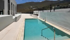 Une piscine à l’eau d’un bleu cristallin, entourée d’un bâtiment blanc et avec une montagne en toile de fond.