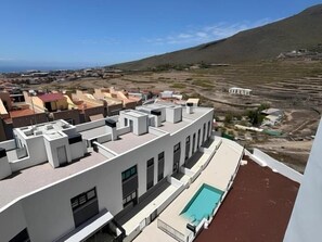 Un bâtiment moderne doté d’une piscine sur le toit, entouré d’un paysage vallonné et d’autres immeubles.