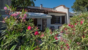 A white building with a tiled roof, surrounded by lush greenery and pink flowers.