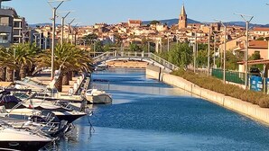 A canal with boats docked on the left, a bridge in the middle, and buildings in the background.