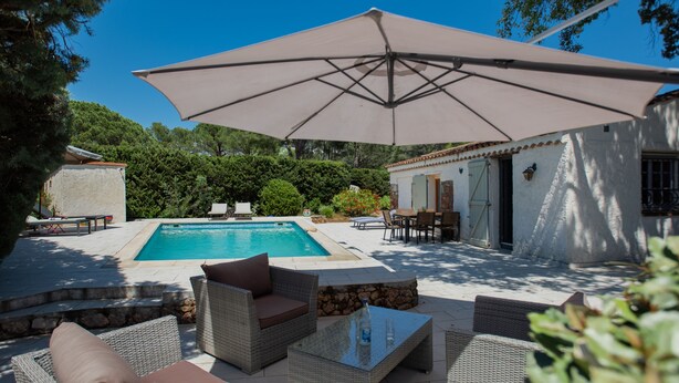 A poolside area with wicker furniture, a table, and a large umbrella.