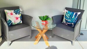 Two wicker chairs with floral cushions, a glass table with wooden legs, and a small potted plant with a red mug on it. - Convenient spot Gosford /near M1HW,CBD,Hospital,Stadium,water view,fishing,pet (West Gosford)