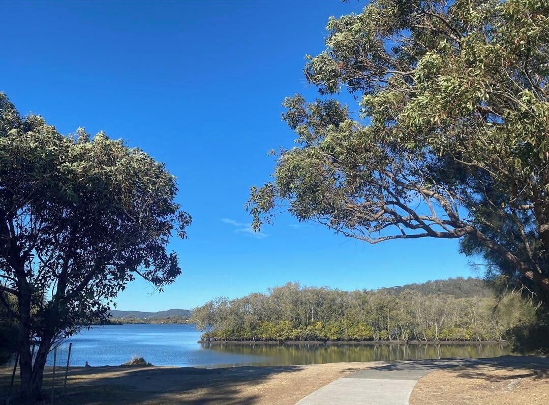 Une vue paisible sur un lac, avec un ciel dégagé, une promenade dallée et une végétation luxuriante.