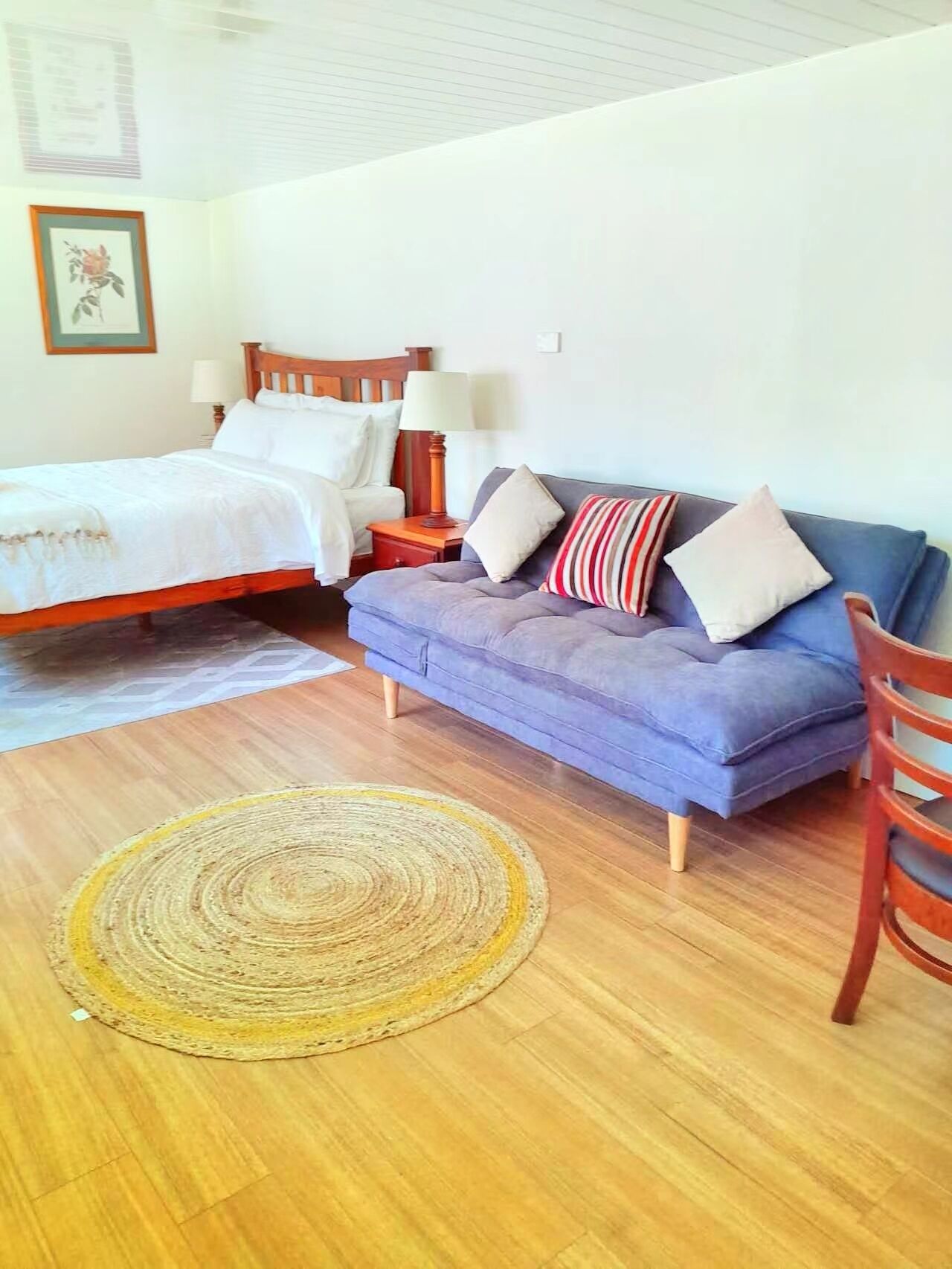 Un dormitorio con una cama, un sofá azul, una silla de madera y un tapiz tejido.
