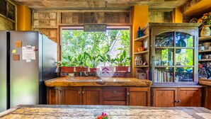A kitchen with wooden cabinets, a stainless steel refrigerator, a wooden countertop, and a window with a view of greenery. - Anam Cara Villa Ubud (Ubud)