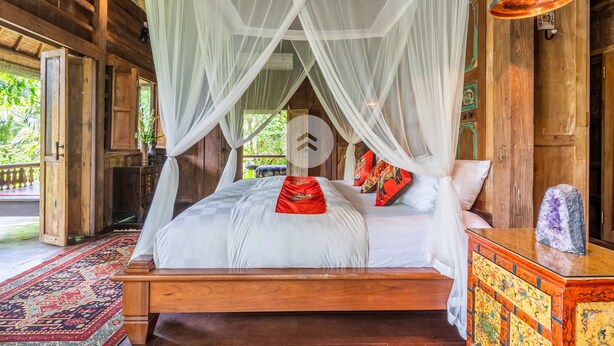 A wooden four-poster bed with a white canopy, a red throw pillow, and a colorful cushion. - Anam Cara Villa Ubud (Ubud)