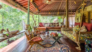 A cozy, rustic room with a wooden ceiling, a sofa with colorful cushions, a wooden bench, and a small table. - Anam Cara Villa Ubud (Ubud)