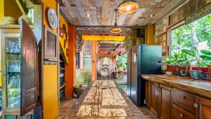 A rustic kitchen with wooden cabinets, a central island, and a view of the outdoors. - Anam Cara Villa Ubud (Ubud)