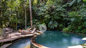 A circular pool with a wooden deck and lounge chairs, surrounded by dense tropical foliage. - Anam Cara Villa Ubud (Ubud)