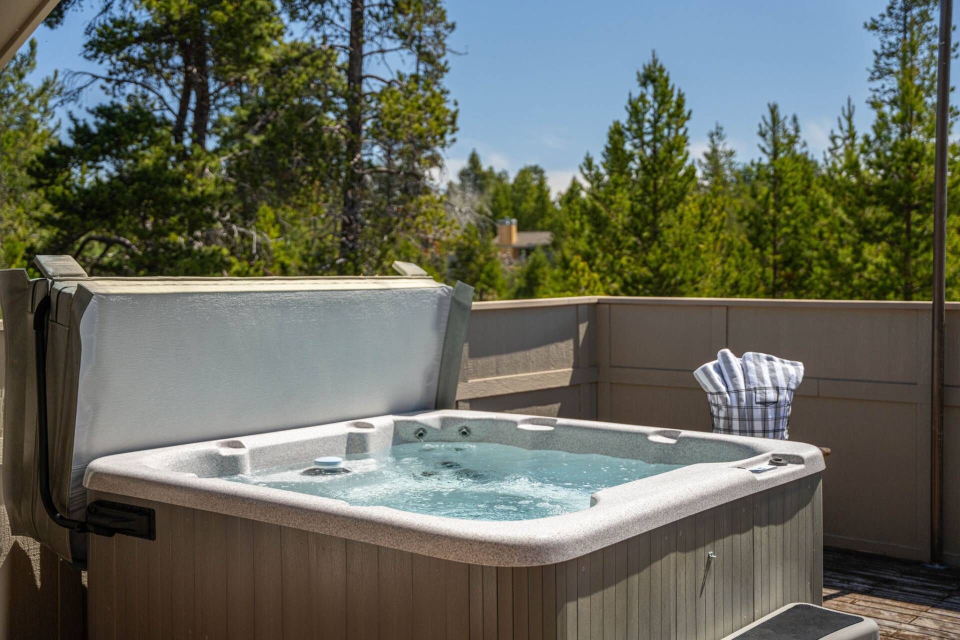 A hot tub on an outdoor deck with a wooden railing, surrounded by trees.