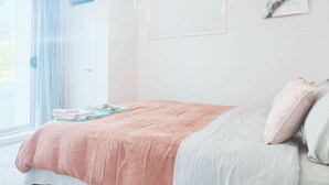 A bedroom with a bed, a window with curtains, a wall-mounted artwork, and a door. - 2 bedroom cosy guest house in North shore (Auckland)