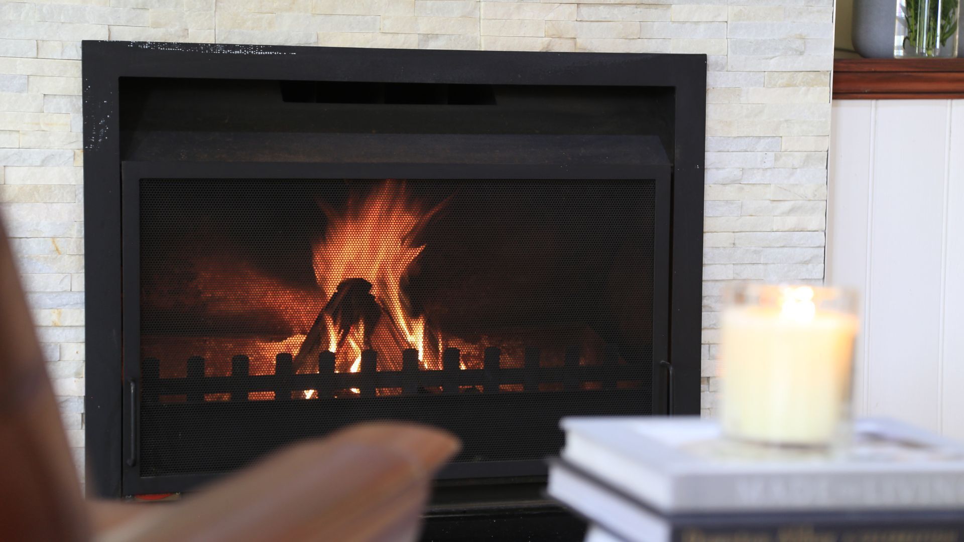 A fireplace with a visible fire, a candle on a table, and a brick wall.