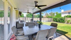 Une terrasse extérieure avec une table et des chaises, un ventilateur de plafond et une vue sur le jardin.