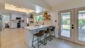 Une cuisine moderne dotée d’un îlot central, de tabourets de bar et offrant une vue sur l’extérieur grâce à de grandes portes coulissantes.