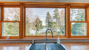 A kitchen with a double sink, wooden window frames, and a view of trees and a lake. - Chic Addison Home w/ Fire Pit on 8 Private Acres! (Addison)