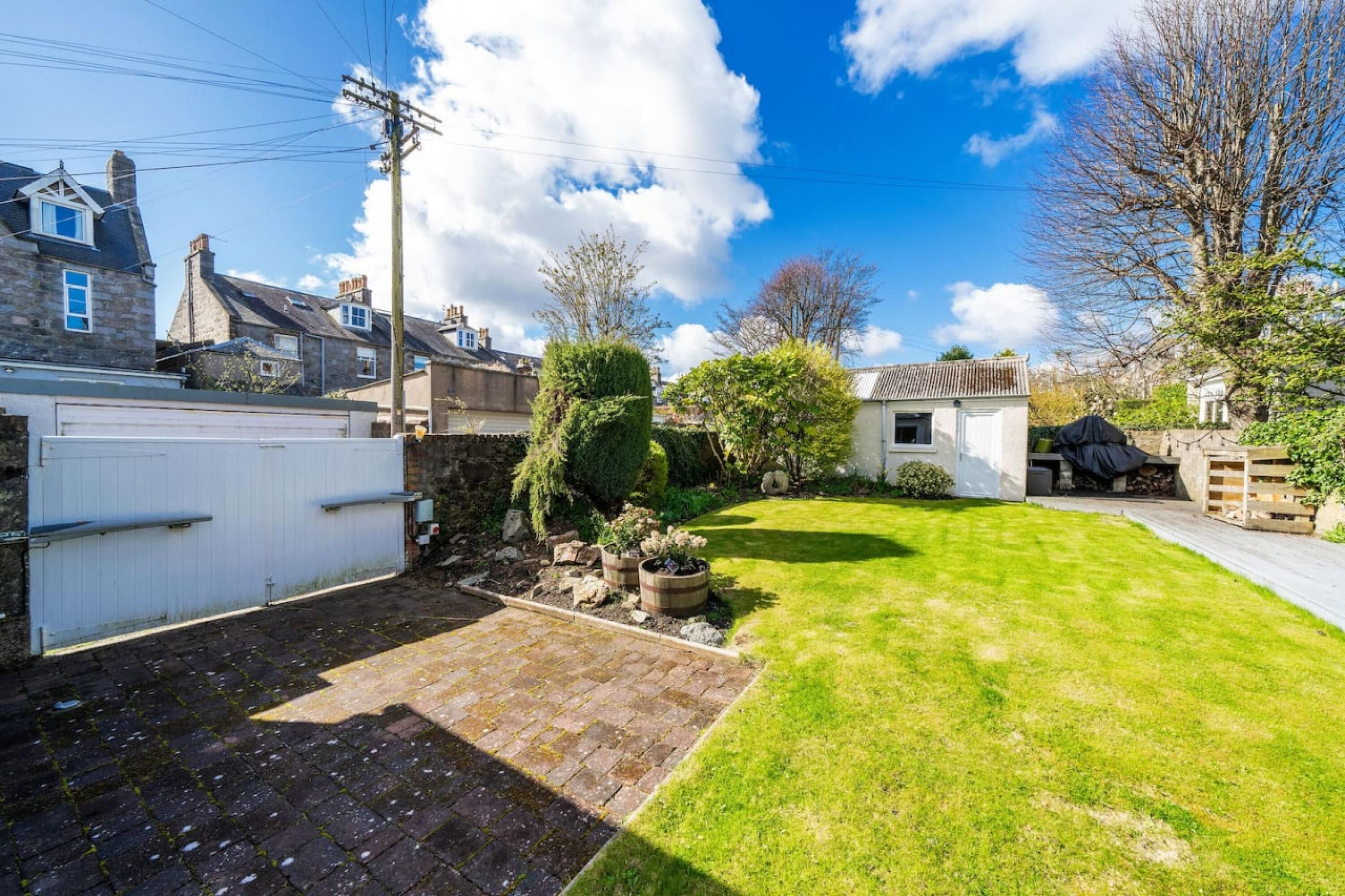A residential property with a paved driveway, a well-maintained lawn, and a small garden area with potted plants.