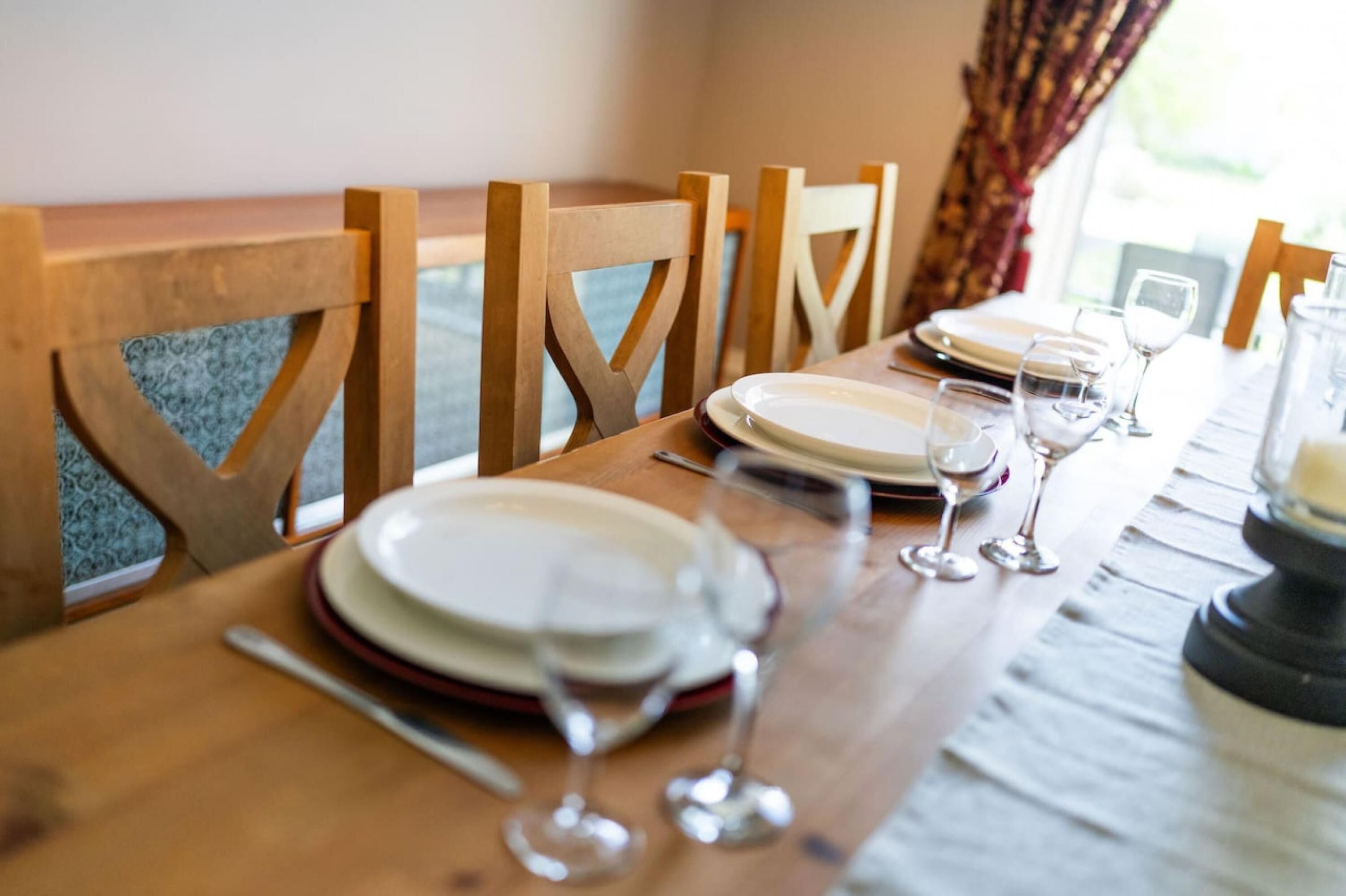 Una mesa de comedor dispuesta con platos, cubiertos y copas de vino, rodeada de sillas de madera.