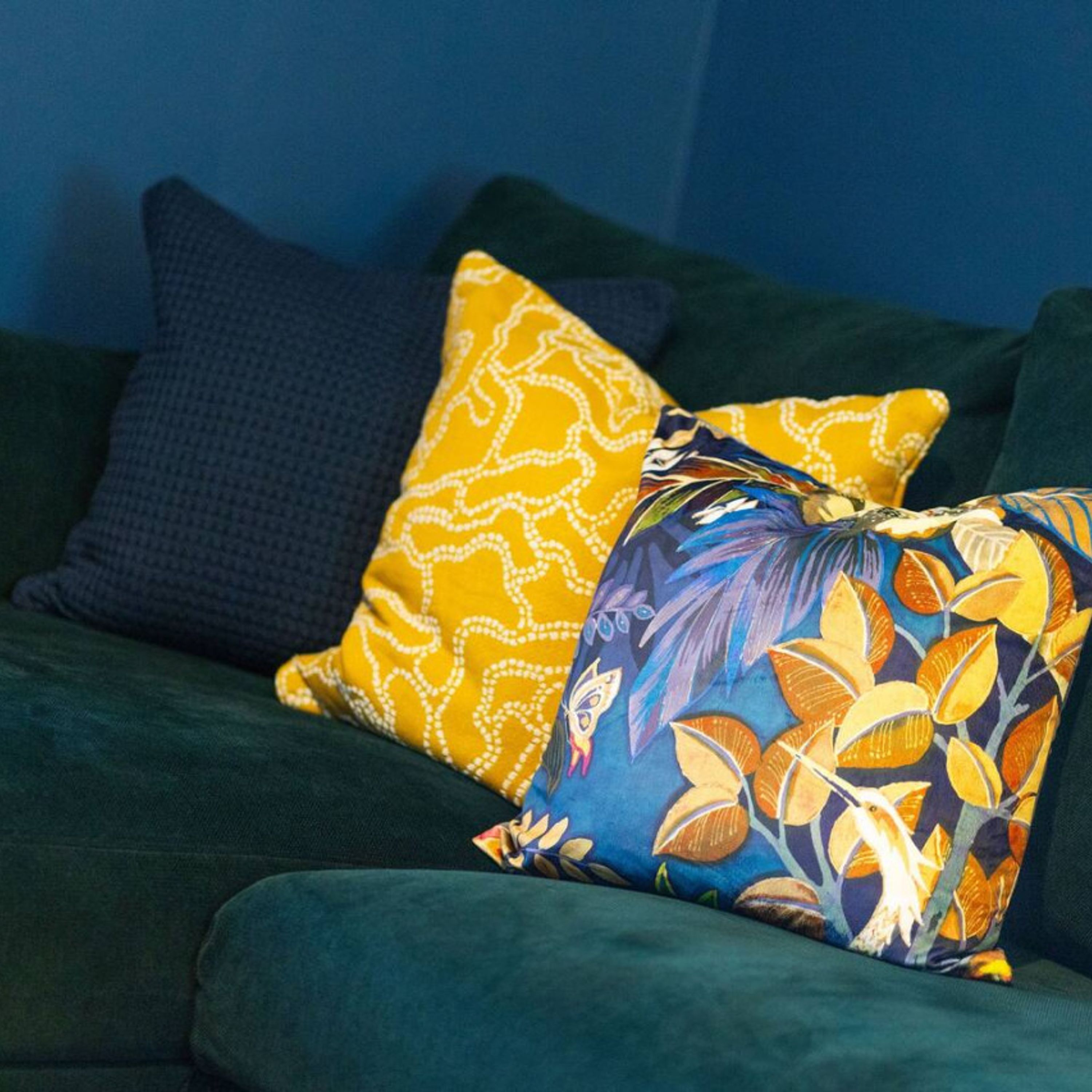 A dark green sofa with two decorative pillows, one with a yellow and white pattern and the other with a colorful floral design.