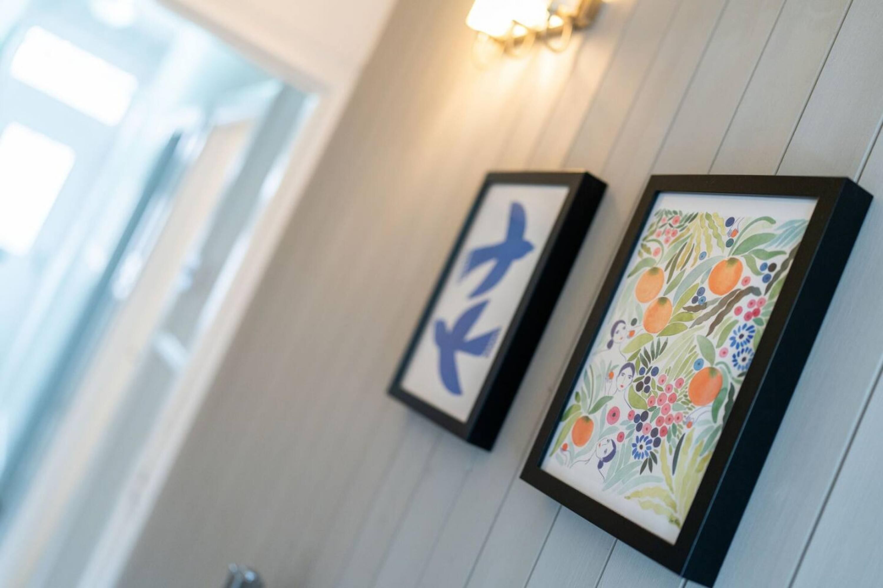 Two framed artworks on a wall with a light fixture above them.