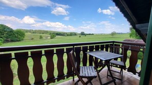 Un balcon avec une table et des chaises, donnant sur un paysage verdoyant.